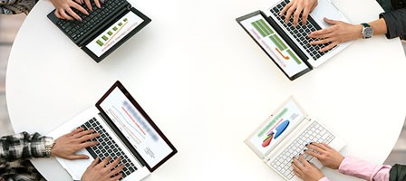 four people sitting at a table working on their laptops