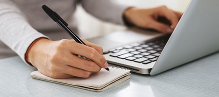 a woman writing in a notebook and working on her laptop