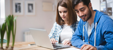 a man and woman looking at a laptop and documents next to them