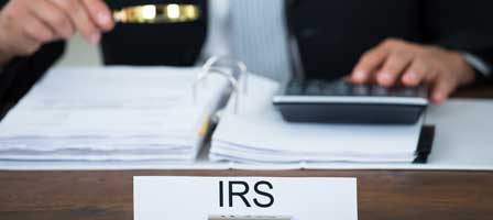 a person sitting at a desk with a name plate that says IRS