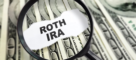 a magnifying glass looking a paper that says roth ira with a stack of money behind it