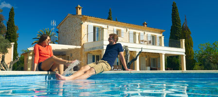 a man and woman sitting at a pool behind a house