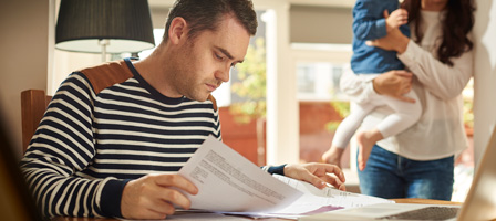 a man looking at paperwork with a woman holding a child in the background