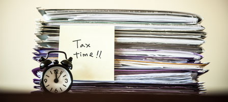 an alarm clock with files behind it and a sticky note that says tax time