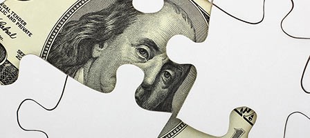 puzzle pieces on top of a hundred dollar bill