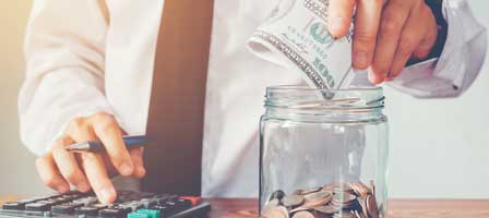 a man pitting a 100 dollar bill in a change jar while using a calculator