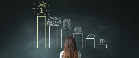 a woman standing in front of a chalk board with different sizes of money stacked in decending order