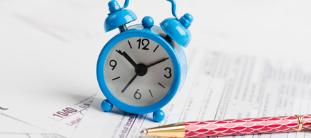 an alarm clock and pen on top of tax paperwork