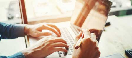 a person working on their laptop with someone else pointing something out on the screen