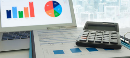 a calculator on top of paperwork with a laptop open in the background