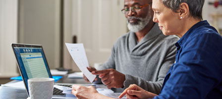 a man and woman going over paperwork together with a laptop in front of them