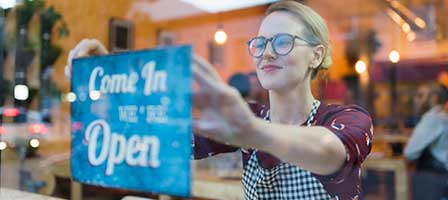 a woman putting up a sign that says come in were open