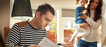 a man looking at paperwork with a woman holding a toddler in the background